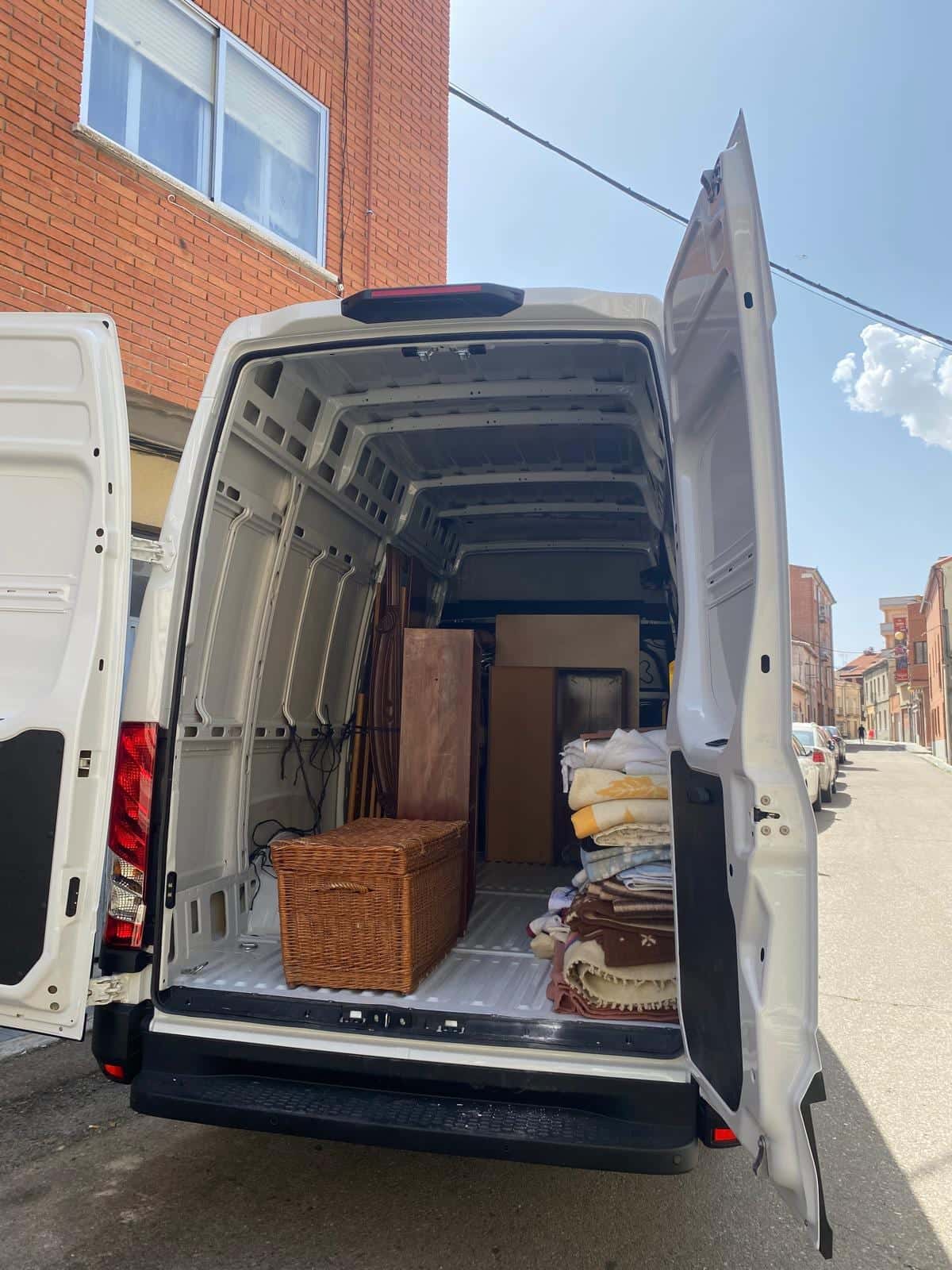 Furgoneta con las puertas traseras abiertas, cargada con un arcón de madera, muebles y bultos protegidos con mantas
